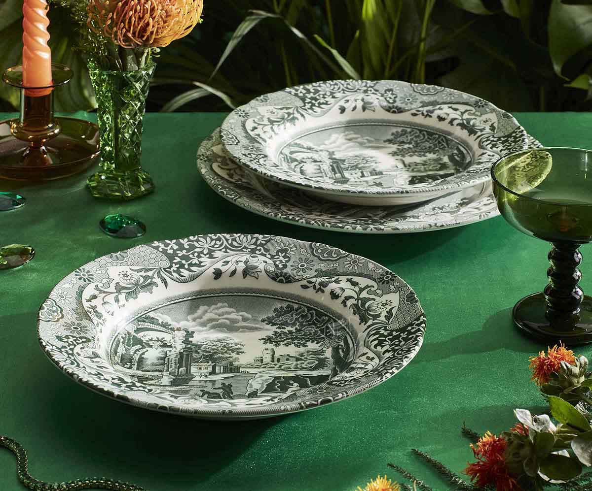Elegant Spode transferware plates with black and white scenic designs displayed on green surface with vintage glassware and floral arrangements